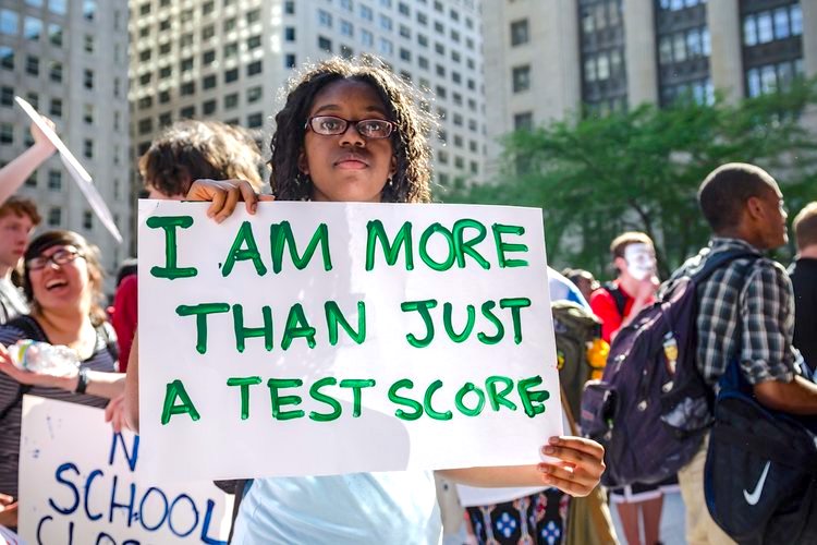 Photo of a youth leader with Providence Student Union holding a sign reading "I am more than just a test score."